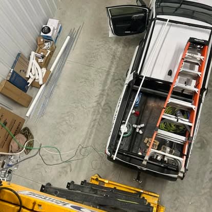Overhead view of a work truck with tools, ladder, and equipment in a garage setting.