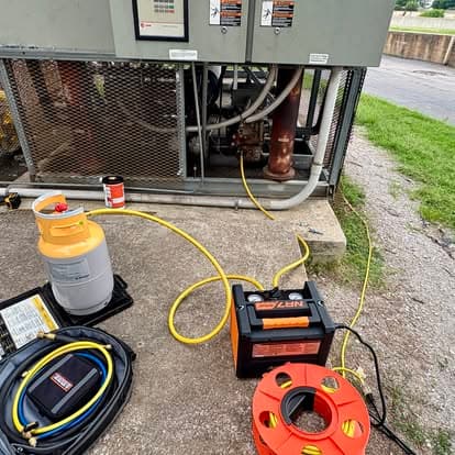 HVAC maintenance tools including refrigerant tank and power source near equipment unit.