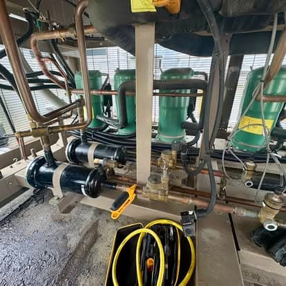 Industrial refrigeration system with green compressors and copper piping, showcasing mechanical details.