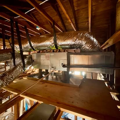 HVAC system installation in attic with ductwork and wooden support beams.